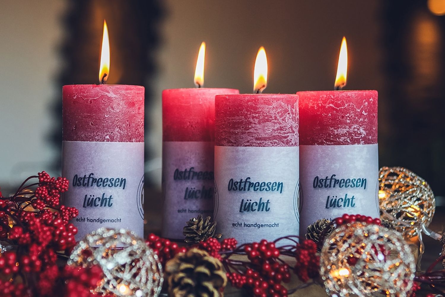 Vier rote Rundkerzen Modell Ostfreesen Lücht, umgeben von Winterdeko in abgedunkeltem Raum.
