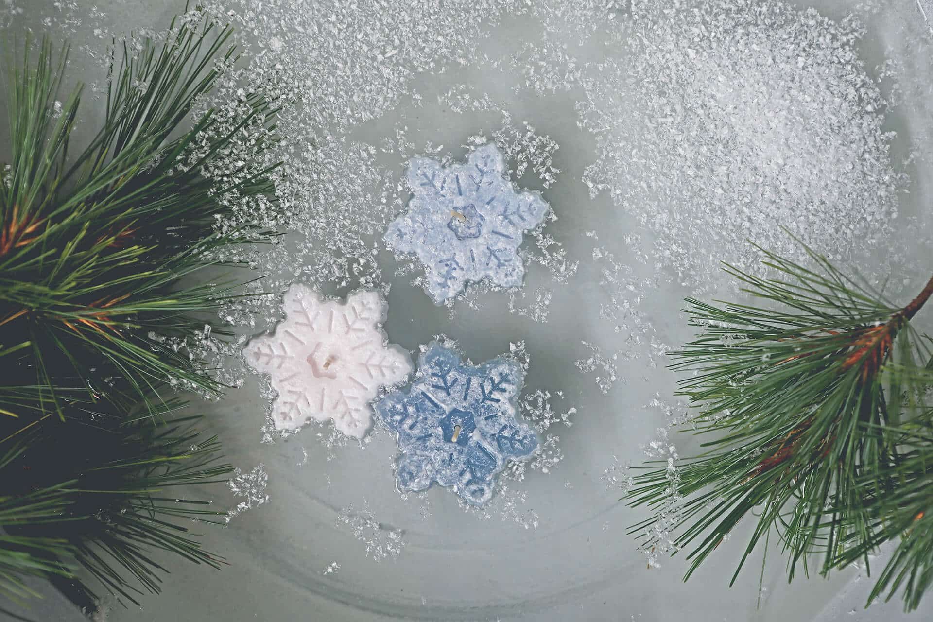 Drei Schwimmkerzen in Form von Schneekristallen, in einer Glasschale mit Wasser schwimmend, in verschiedenen Blautönen.