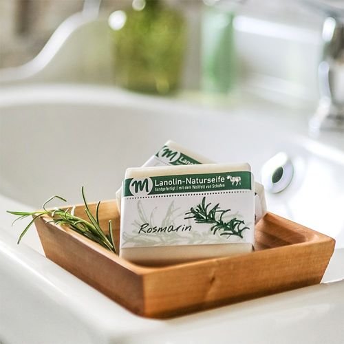 Lanolin-Naturseife mit Rosmarin-Duft, auf einer Seifenschale aus Holz.