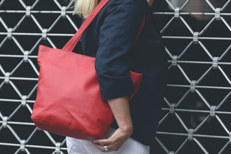 Eine Person trägt eine Handtasche aus Leder in der Farbe corallrot über der Schulter.