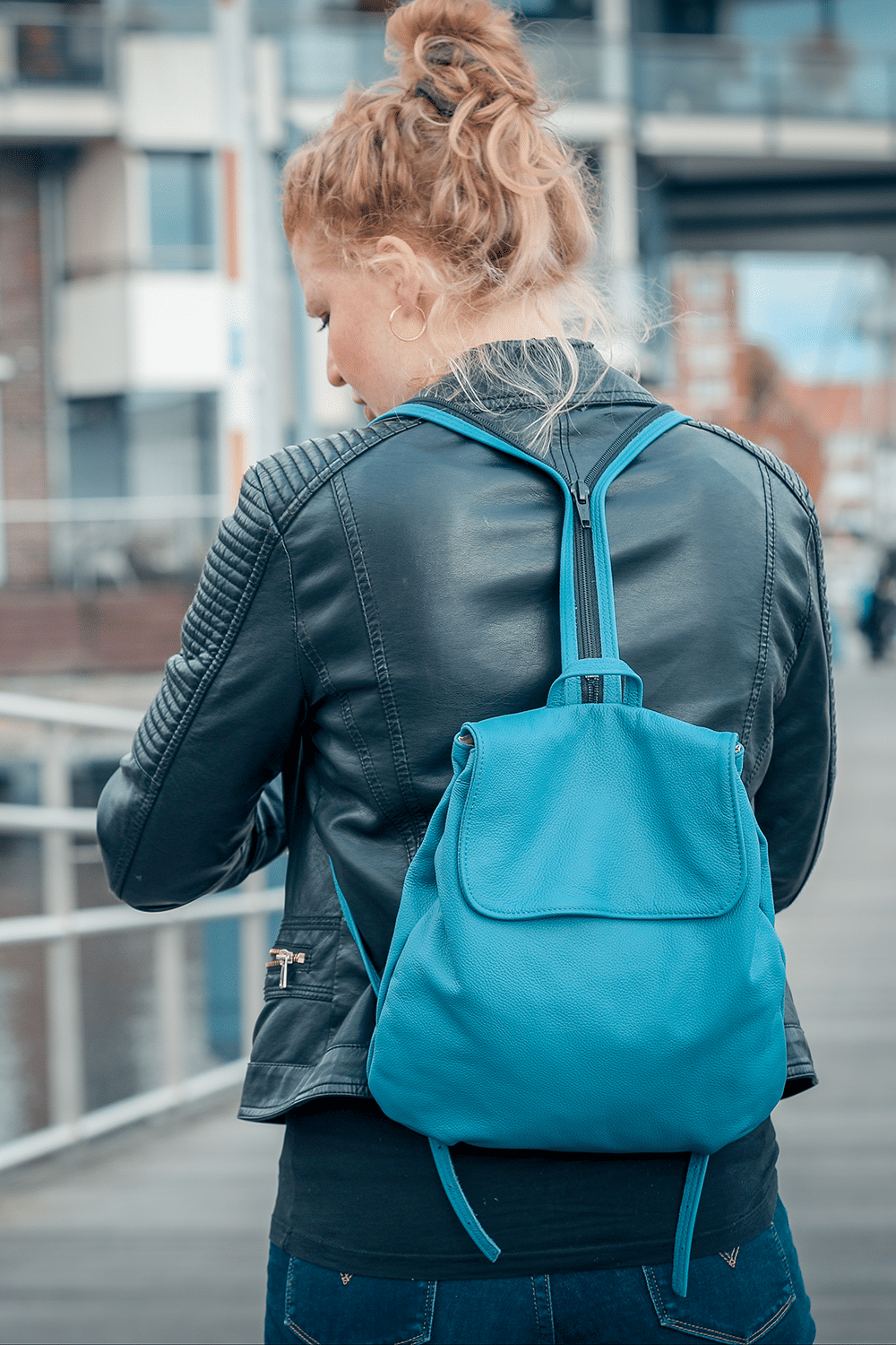 Eine Person trägt einen kleinen Rucksack aus Leder in der Farbe rauchblau auf dem Rücken.