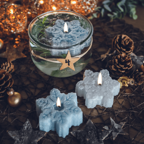 Drei Schwimmkerzen in Form von Schneekristallen, eine in einer Glasschale mit Wasser schwimmend, in verschiedenen Blautönen.