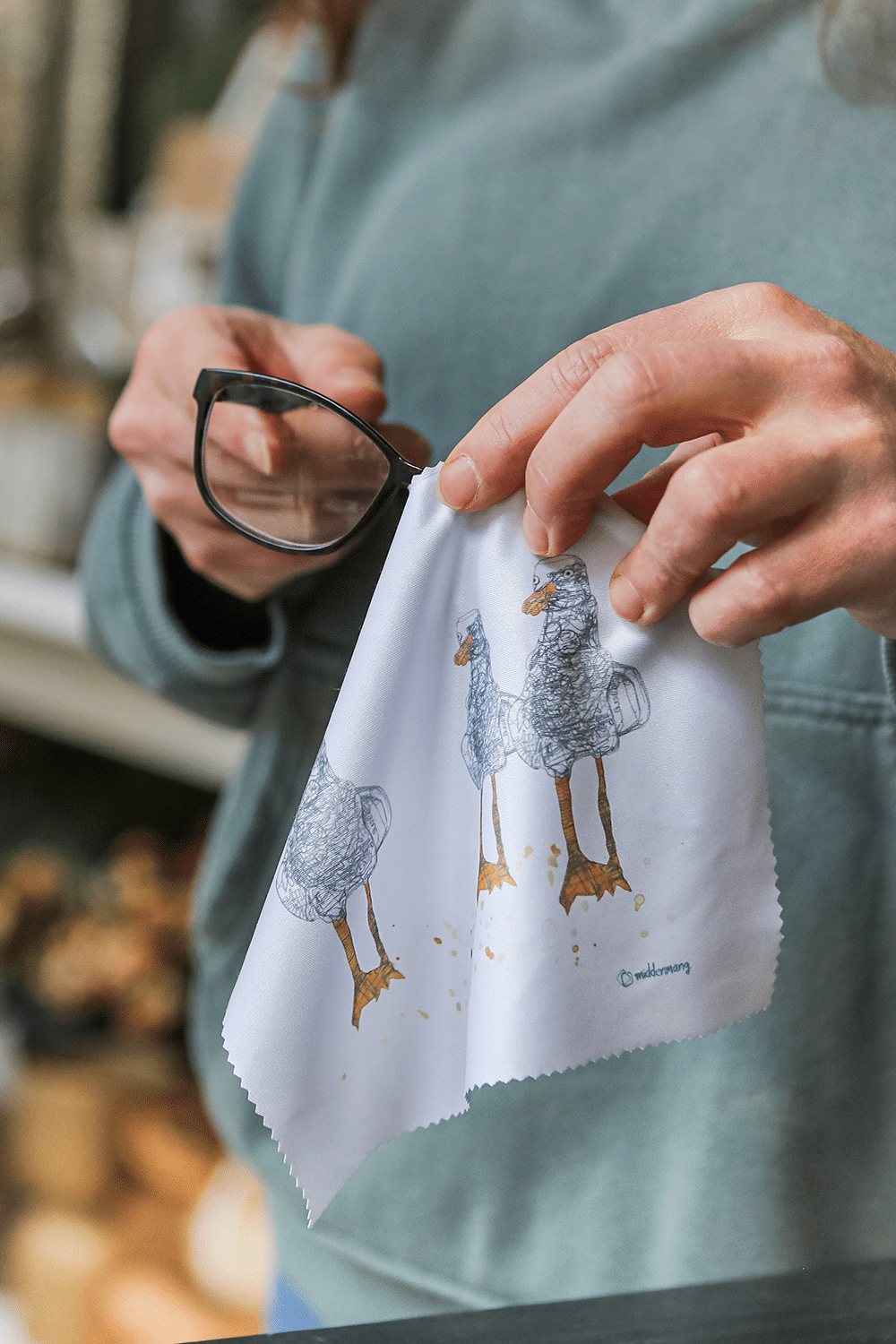 Eine Person putzt mit dem Brillenputztuch mit drei kunstvollen Möwen eine Brille.