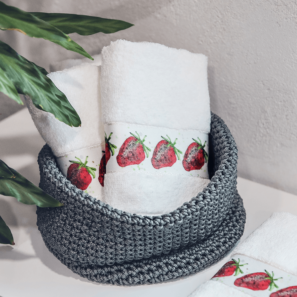 Zwei Handtücher in einem grauen Korb, bedruckt mit Erdbeeren.