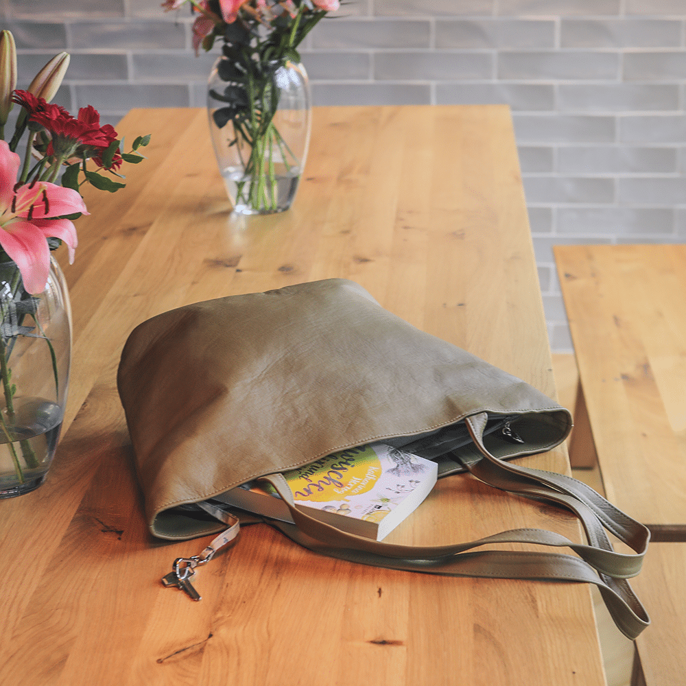 Eine große Shopping-Ledertasche in der Farbe oliv liegt auf einem Tisch.