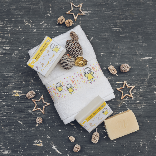 Lanolin-Naturseife mit Apfel-Zimt-Duft und einer Banderole mit duftigem Engel auf einem Gästehandtuch mit Engel-Motiv.