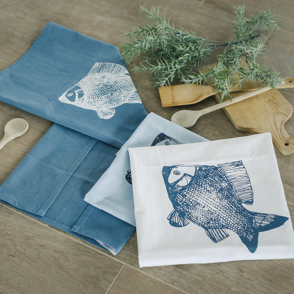 Drei Geschirrtücher, bedruckt mit Fischen, liegen gefaltet neben- und aufeinander.