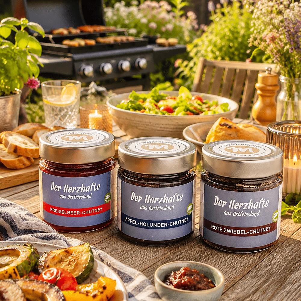 Drei verschiedene Chutneys auf einem Gartentisch, mit einem Grill im Hintergrund.