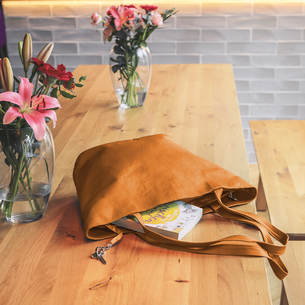 Eine große Shopping-Ledertasche in der Farbe goldbraun liegt auf einem Tisch.