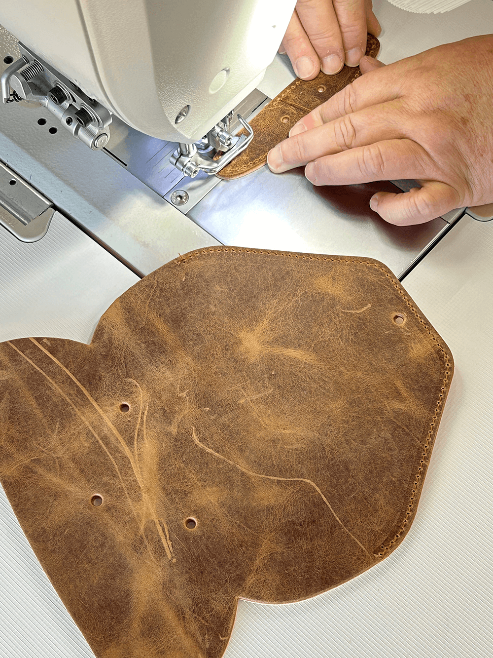 Eine Person bearbeitet mit einer Nähmaschine ein Stück hellbraunes Leder.