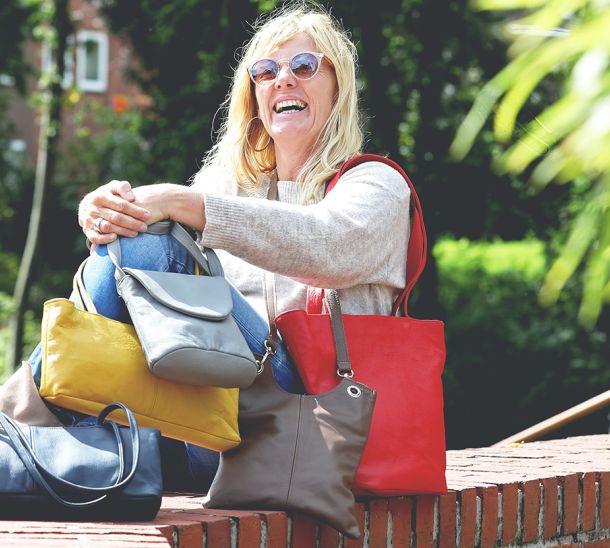 Eine Person sitzt auf einer Mauer mit verschiedenen Taschen aus Leder in verschiedenen Farben.