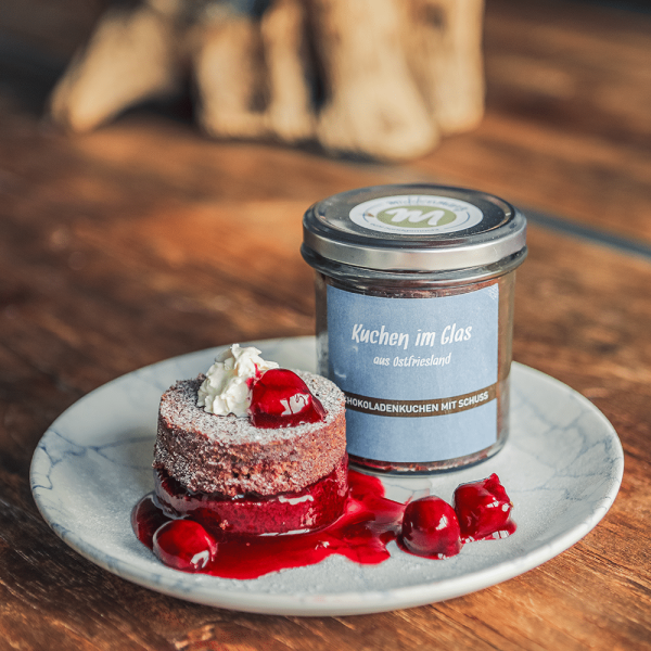 Schokoladenkuchen mit Schuss, in Scheiben geschnitten und auf einem Teller mit Kirschen, Sahne und Puderzucker angerichtet.