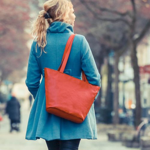 Eine Person tr&auml;gt eine Tasche aus Leder in rot &uuml;ber der Schulter.