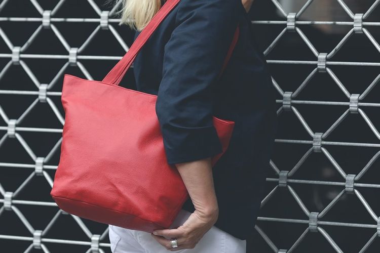 Eine Person trägt eine Handtasche aus Leder in der Farbe corallrot über der Schulter.