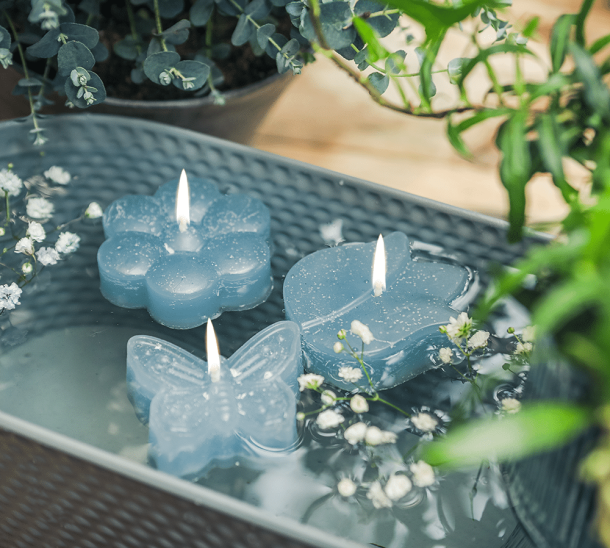 Drei Schwimmkerzen in den Formen Schmetterling, Tulpe und Blume in der Farbe Wasser, in einer Schale schwimmend.