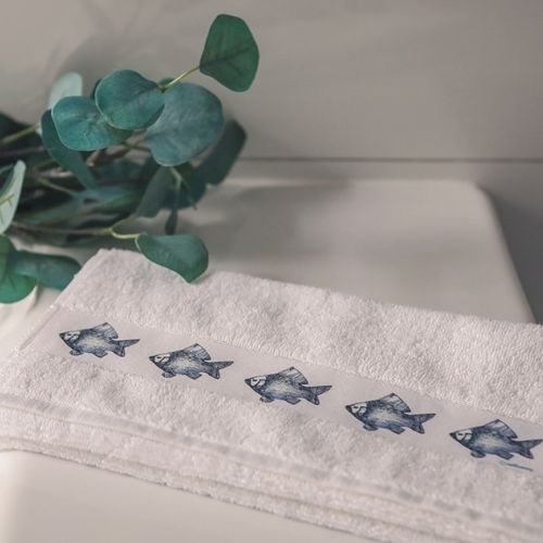 Eine Person reinigt ein Glas mit einem hellblauen Geschirrtuch mit dunkelblauem Fisch-Motiv.