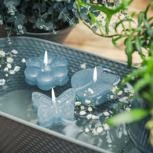 Drei Schwimmkerzen in den Formen Schmetterling, Tulpe und Blume in der Farbe Wasser, in einer Schale schwimmend.