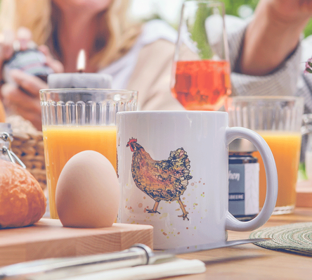 Tasse mit dem Motiv Huhn auf gedecktem Frühstückstisch.