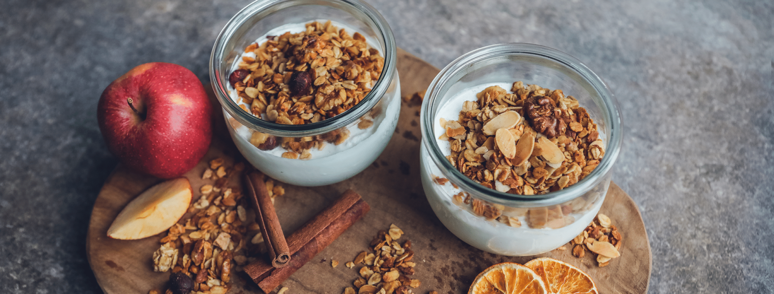 Knuspermüsli Apfel-Zimt steht im Garten auf Holzkiste neben Äpfeln und einer Schale Müsli.