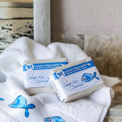 Zwei Stücke Seife liegen auf einem Handtuch mit dem Motiv Fisch in einem Badezimmer.