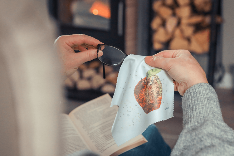 Eine Person reinigt eine Brille mit einem Brillenputztuch, bedruckt mit einem Apfel.