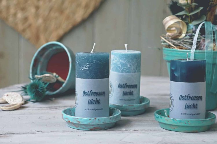 Drei Rundkerzen in Blautönen mit der Aufschrift Ostfreesen Lücht stehen auf Tisch mit Deko.