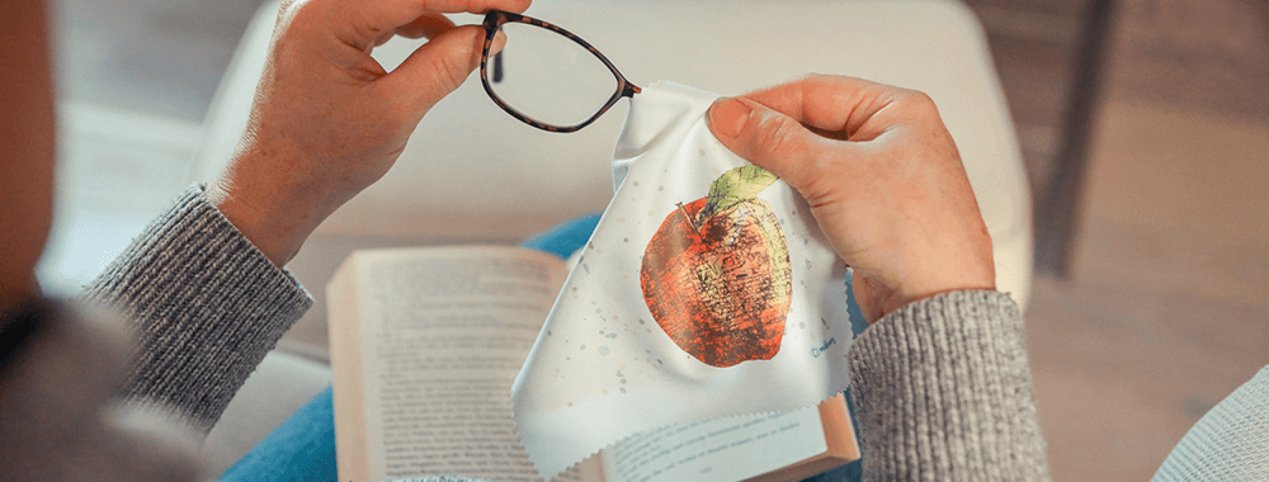 Eine Person reinigt eine Brille mit einem Brillenputztuch, bedruckt mit einem Apfel.