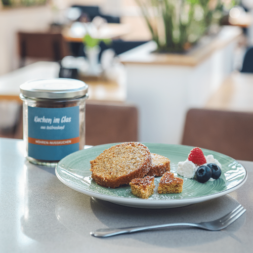 Möhren-Nusskuchen, in Scheiben geschnitten auf einem Teller angerichtet, mit Puderzucker, Sahne und Beeren.