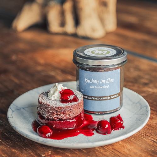 Schokoladenkuchen mit Schuss, in Scheiben geschnitten und auf einem Teller mit Kirschen, Sahne und Puderzucker angerichtet.