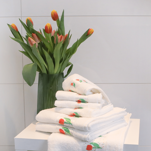 Ein Stapel Handtücher und Gästehandtücher mit Tulpenmotiv, auf einem Hocker, mit einer Vase Tulpen daneben.