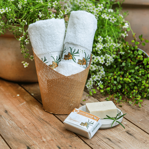 Zwei Gästehandtücher in einem Gefäß, mit Sanddorn bedruckt und mit Sanddornseife daneben.