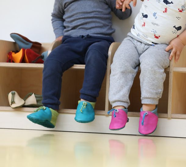 Zwei Babys tragen Babyschuhe aus Leder in unterschiedlichen Farben.