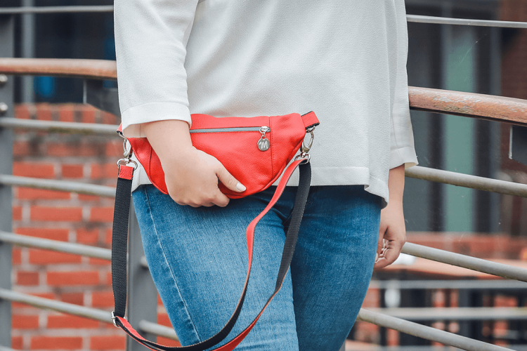 Eine Person trägt eine Bauchtasche auf Leder in der Farbe corallrot.