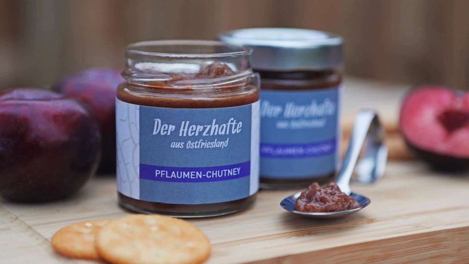 Pflaumen-Chutney mit Crackern und Pflaumen auf einem Holzbrett.