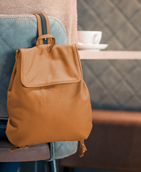 Ein kleiner Rucksack in der Farbe goldbraunhängt über einem Stuhl in einem Restaurant.
