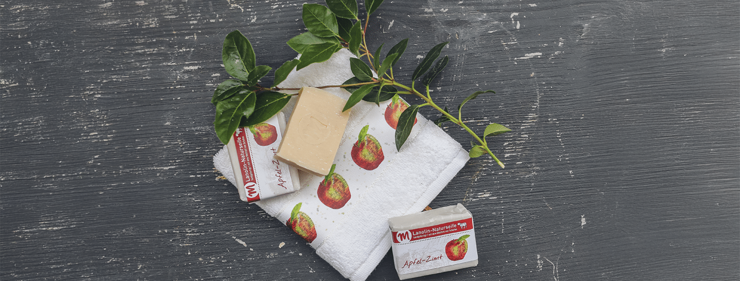 Lanolin-Naturseife mit Apfel-Zimt-Duft, mit grünem Zweig und Gästehandtuch mit Apfel-Motiv.