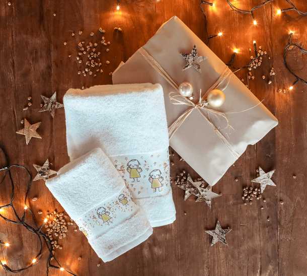 Ein Gästehandtuch und ein Handtuch, bedruckt mit Engeln liegen auf einem Holztisch mit weihnachtlicher Dekoration.