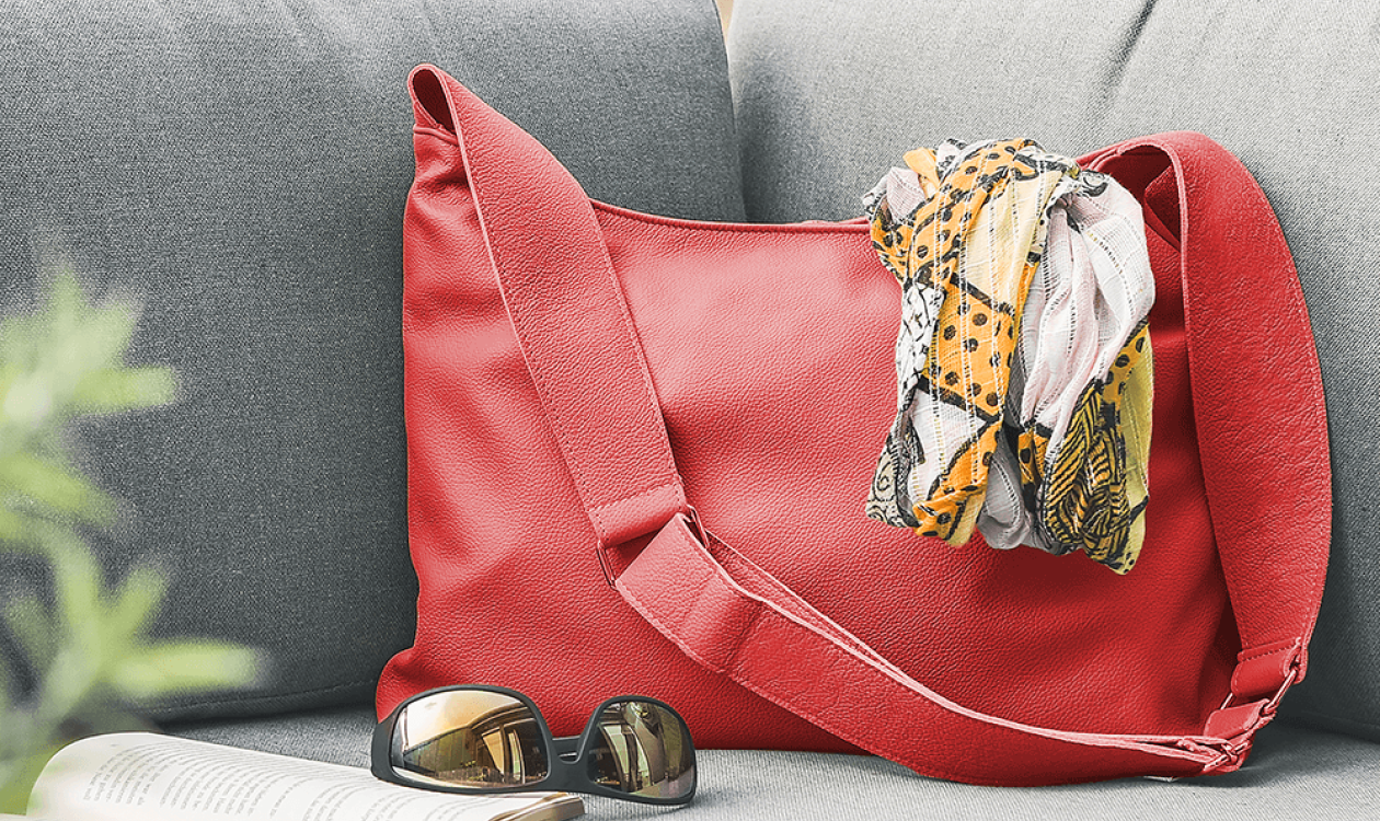 Eine Handtasche aus Leder in der Farbe corallrot liegt auf einem grauen Sofa.