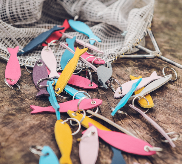 Schlüsselanhänger in Form von Fischen, in verschiedenen Farben aus Leder, dekoriert an einem Fischernetz.