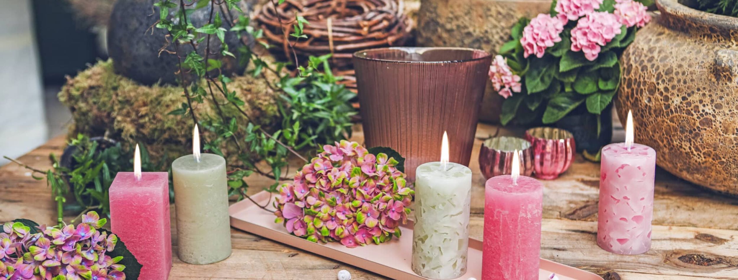 Fünf Stumpenkerzen in den Farben Bubblegum und Avocado, auf einem Holztisch dekoriert mit einem Tablett und Blumen.