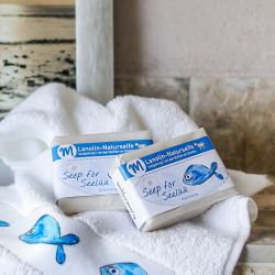 Zwei Stücke Seife liegen auf einem Handtuch mit dem Motiv Fisch in einem Badezimmer.