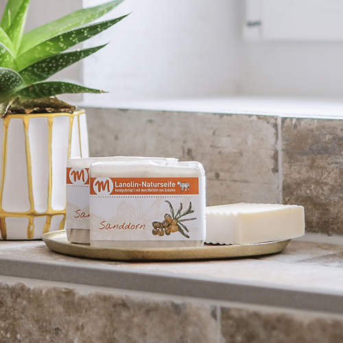 Drei St&uuml;cke Lanolin-Naturseife mit Sanddorn befinden sich auf einem goldfarbenen Tablett.