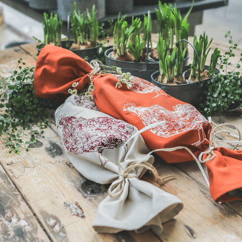Geschirrtuch mit Hühnermotiv, in beige und rost-orange in Geschenkform, mit Pflanzen dekoriert.