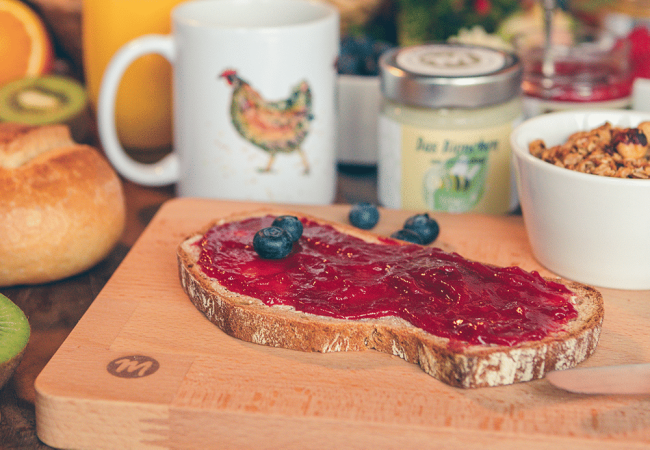 Zwei Frühstückbretter mit dem Motiv Huhn, dekoriert mit Brötchen, Tomaten und einem Ei.