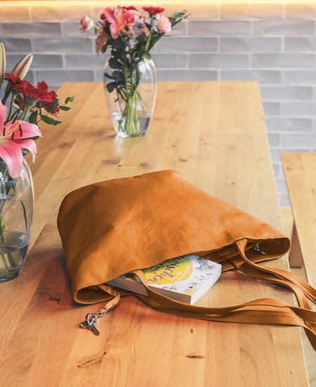 Eine große Shopping-Ledertasche in der Farbe goldbraun liegt auf einem Tisch.
